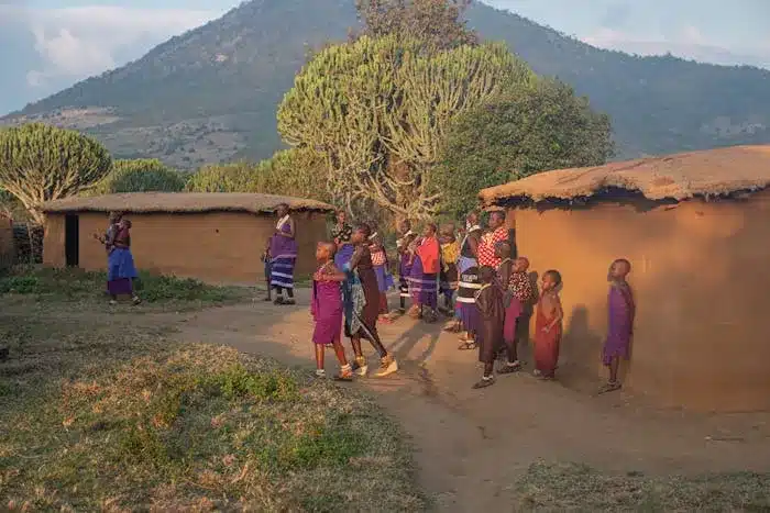 a group of tanzanian  people standing in front of a hut